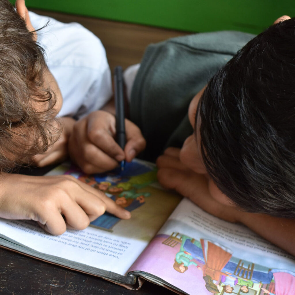 Two young kids look at a workbook and draw on it