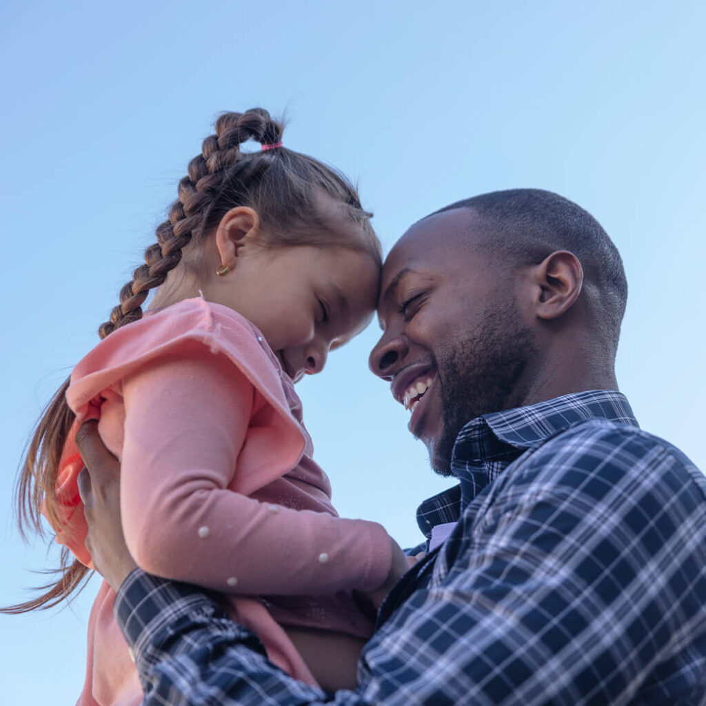 A father holding his daughter up in the air, touching foreheads.